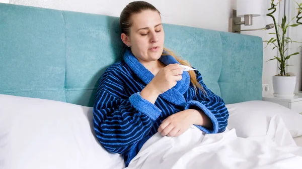Портрет расстроенной женщины с гриппом, смотрящей на цифровой термометр — стоковое фото