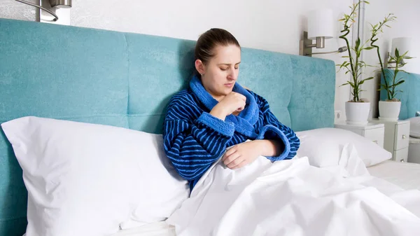 Retrato de una mujer enferma acostada en la cama y tomando termómetro digital debajo del brazo —  Fotos de Stock