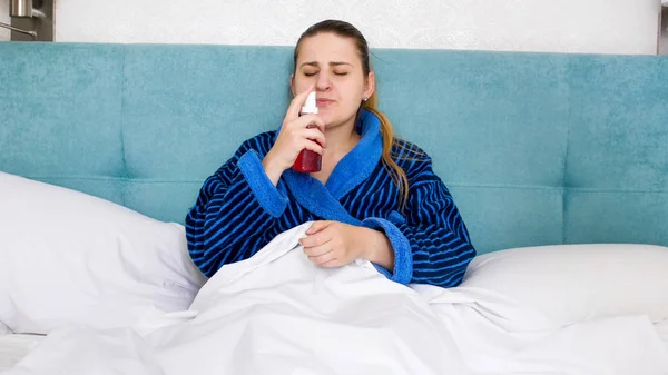 Retrato de una mujer enferma acostada en la cama y usando aerosol de garganta — Foto de Stock