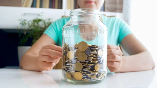 CLoseup photo de femme oyung assis derrière le bureau et regardant sur un pot en verre plein de pièces de monnaie — Photo