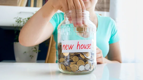 Closeup photo of young woman throwing coin in glass jar with savings for buying new house — Stock Photo, Image