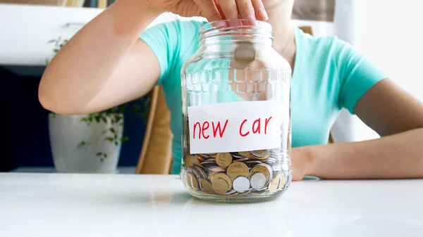 Фотография крупным планом молодой женщины, наполняющей стеклянную банку экономией денег на покупку нового автомобиля — стоковое фото