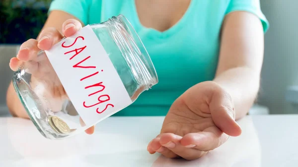 Closeup photo of young woman having financial problems emptying glass jar with money savings — Stock Photo, Image