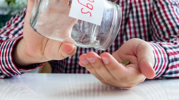 Gambar close-up dari pemuda menuangkan beberapa koin di tangan untuk botol kaca dengan tabungan uang — Stok Foto