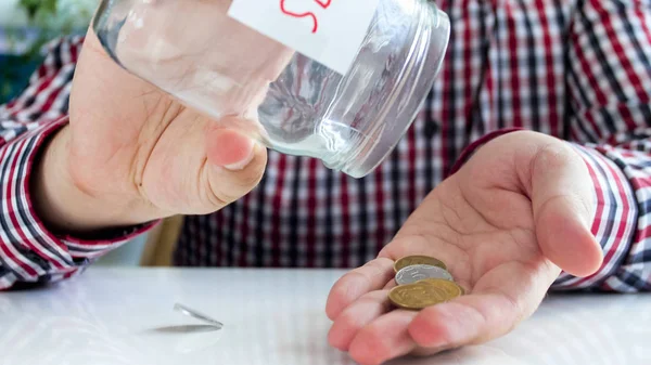 Imagem de perto do jovem derramando algumas moedas de frasco de vidro com economia de dinheiro — Fotografia de Stock