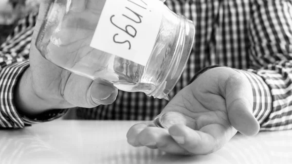 Black and white image of young man emptying glass jar with money savings — Stock Photo, Image