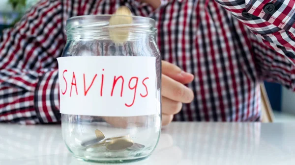 Closeup image of young man filling glass jar for savings with money — Stock Photo, Image