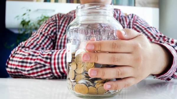 Closeup image of young man holding glass jar with money savings — Stock Photo, Image