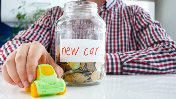 새 차를 구입 하는 젊은 남자의 근접 촬영 사진입니다. 항아리 가득 흰색 테이블에 돈 및 소형 장난감 자동차 — 스톡 사진