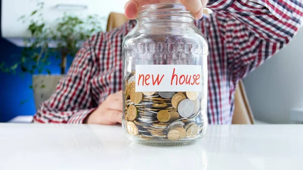 Imagem de close-up do jovem segurando frasco de vidro com economia de dinheiro para a compra de nova casa — Fotografia de Stock