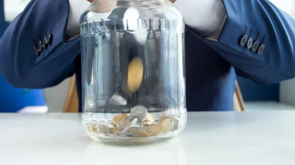 Closeup image of young businessman filling glass jar with coins — Stock Photo, Image