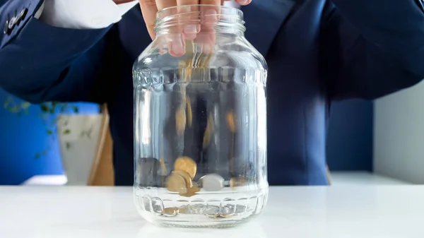Φωτογραφία: closeup νέος επιχειρηματίας που ρίχνουν κέρματα σε γυάλινο βάζο — Φωτογραφία Αρχείου