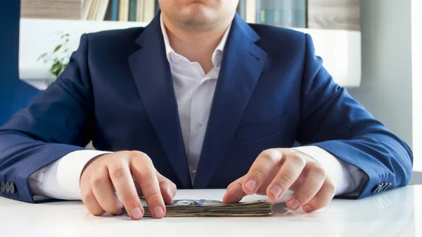 Imagem de close-up do jovem empresário segurando grande pilha de dinheiro sentado atrás da mesa de madeira branca no escritório — Fotografia de Stock