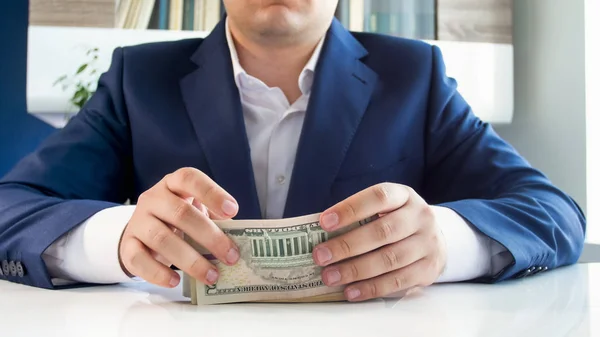 Closeup image of young successful businessman sitting behind desk and holding big stack of money — Stock Photo, Image