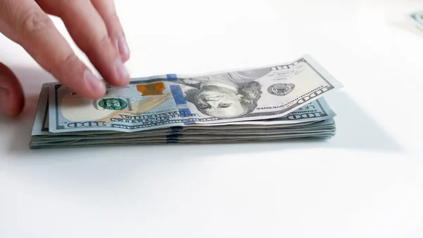 Closeup image of hand taking stack of dollars lying on hwite wooden desk — Stock Photo, Image