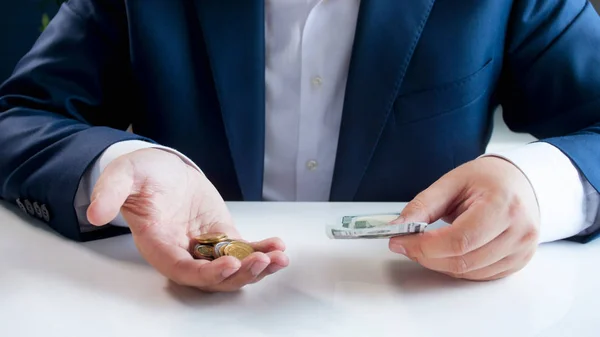 Nahaufnahme eines Geschäftsmannes, der hinter seinem Schreibtisch sitzt und Kreditkarten und Metallmünzen in der Hand hält — Stockfoto