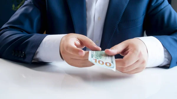 Imagen de primer plano del hombre de negocios sentado detrás del escritorio y con una factura de 100 dólares estadounidenses — Foto de Stock