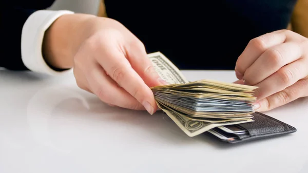 Closeup image of young businesswoman putting big stack of money in leather wallet — Stock Photo, Image