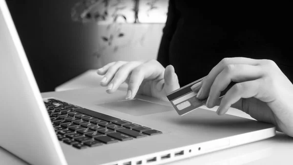 Black and white image of young woman typing on laptop and holding credit card in hand — Stock Photo, Image