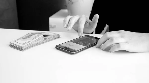 Imagen en blanco y negro de la mujer usando la calculadora de teléfonos inteligentes mientras cuenta el dinero — Foto de Stock