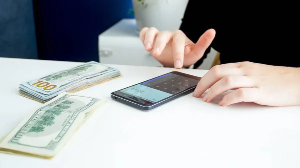 Imagen de primer plano de la mujer de negocios que usa el teléfono inteligente mientras cuenta una gran cantidad de dinero —  Fotos de Stock