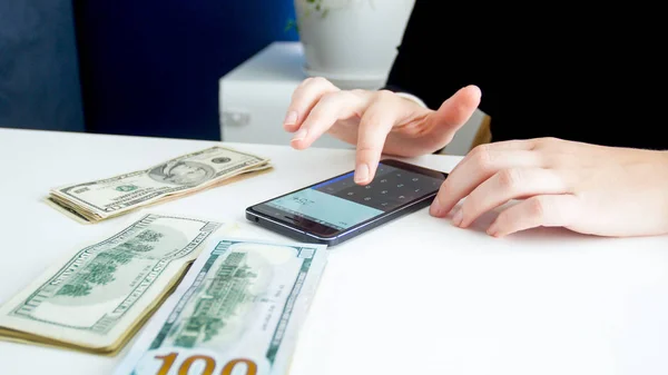 Imagen de primer plano del banquero femenino usando un teléfono inteligente mientras cuenta el dinero —  Fotos de Stock