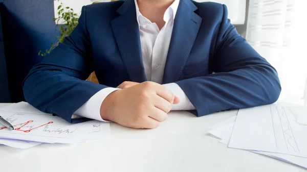 Imagen de primer plano del hombre de negocios en traje azul sentado detrás de un escritorio cubierto de gráficos y gráficos —  Fotos de Stock