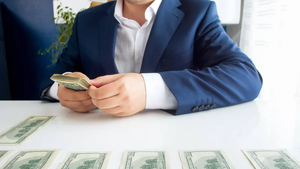 Closeup image of businessman sitting behind desk and laying stack of money in front of him — Stock Photo, Image