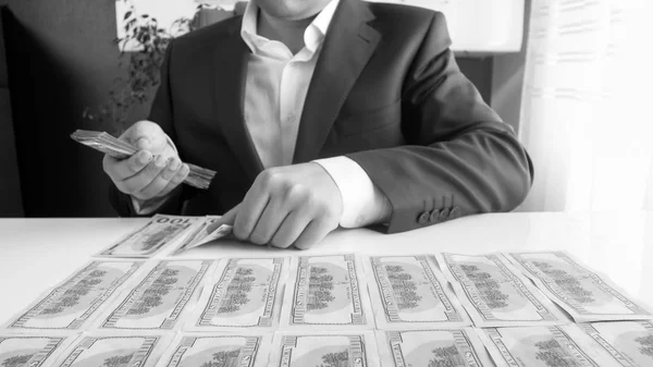 Imagen en blanco y negro del hombre de negocios sentado detrás del escritorio y depositando dinero en filas —  Fotos de Stock