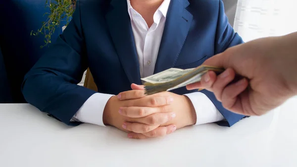 Imagem de perto de mão segurando pilha de dinheiro que se estende para homem de negócios sentado no escritório — Fotografia de Stock