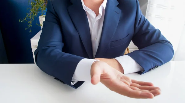 Imagem de perto do empresário sentado atrás da mesa de escritório estendendo a mão e pedindo dinheiro — Fotografia de Stock