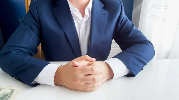 在现代办公室用折叠的手坐在蓝色西装的富有的成功的商人特写形象 — 图库照片