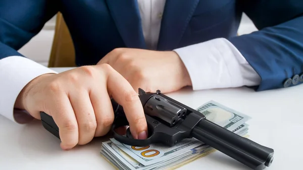 Closeup image of businessman with stack of money and gun sitting behind office desk — Stock Photo, Image