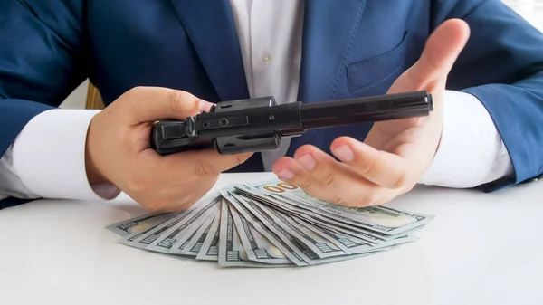 Closeup photo of businessman holding revolver and looking at big stack of money — Stock Photo, Image