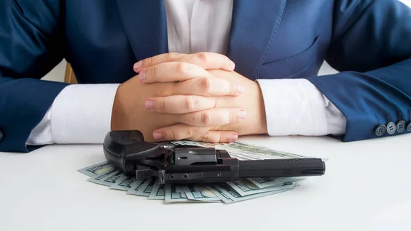 Closeup photo of businessman sitting in front of revolver lying on stack of money — Stock Photo, Image