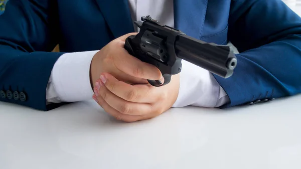 Closeup image of man in suit sitting behind office desk and aiming with revolver — Stock Photo, Image