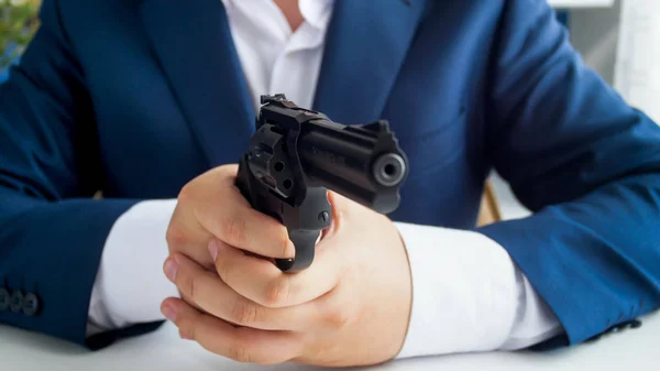 Closeup photo of man in suit sitting in armchair at office and aiming with gun — Stock Photo, Image