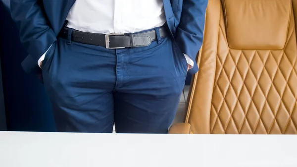 Closeup image of businessman in blue suit standing in office next to brown leather armchair — Stock Photo, Image