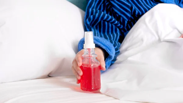 Närbild bild av sjuk kvinna ligger i sängen och tar öm hals spray — Stockfoto