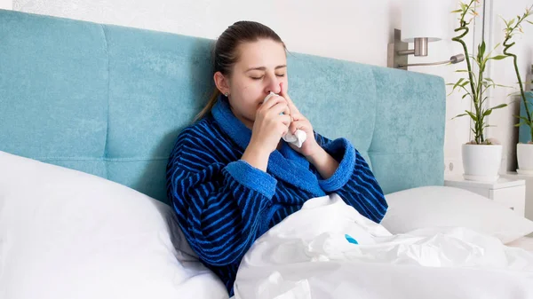 Retrato de jovem doente com gripe deitada na cama e usando spray nasal — Fotografia de Stock