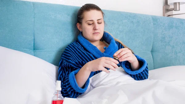 Молодая больная женщина лежит в постели и открывает бутылку с лекарством — стоковое фото