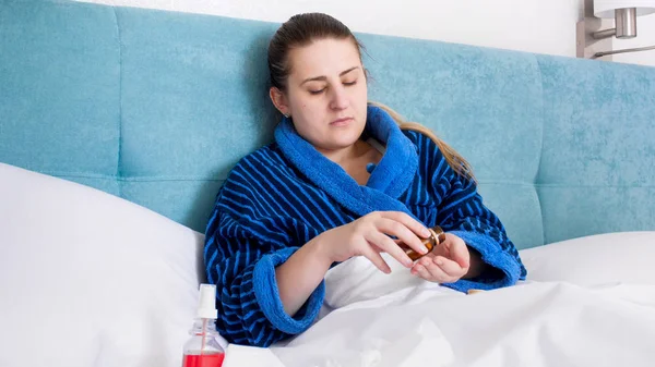 Portrait of sick woman with cold lying in bed and pouring pills on hand — Stock Photo, Image