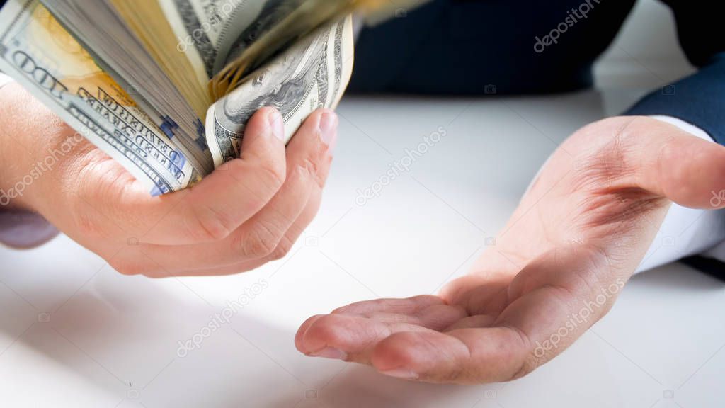 Closeup image of man in suit slapping big stack of money on hand