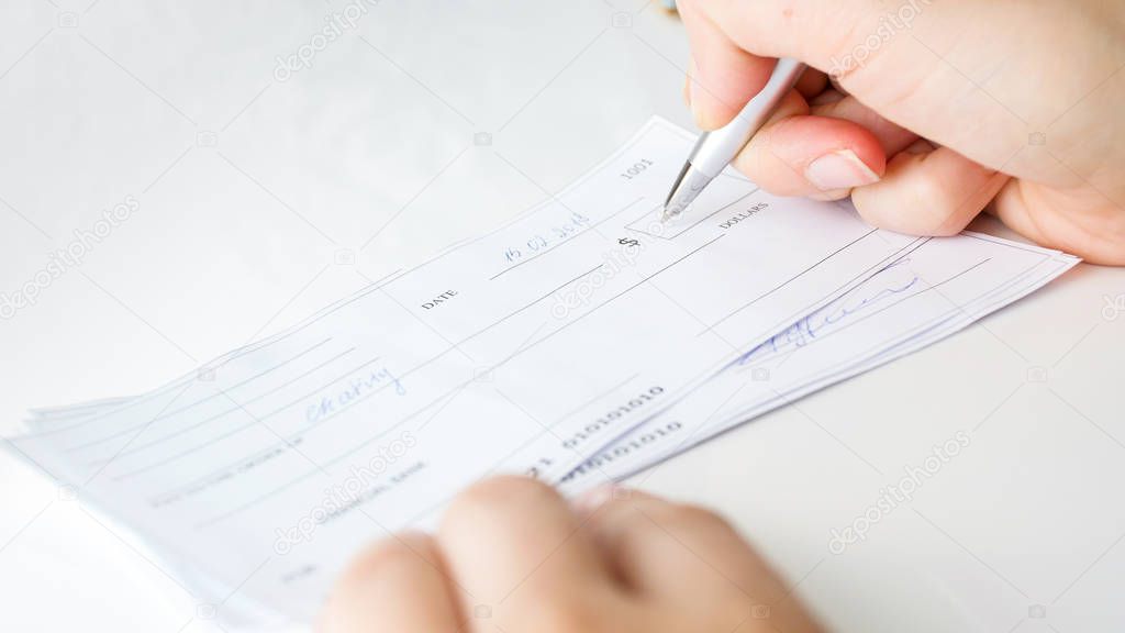 Closeup image of person filling money amount on personal bank cheque