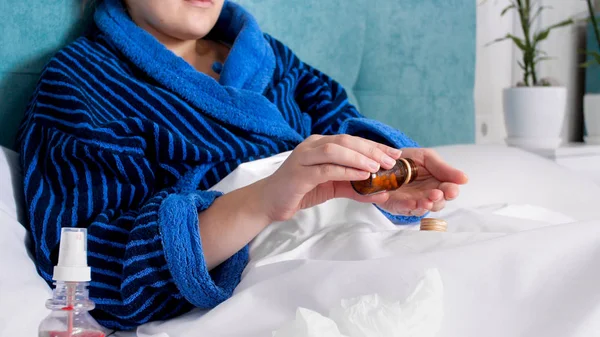 Closeup image of sick woman in bathrobe lying in bed and holding pills and medicines — Stock Photo, Image
