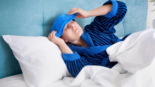 Retrato de una joven enferma que sufre de migraña poniendo toalla fría húmeda en la frente — Foto de Stock