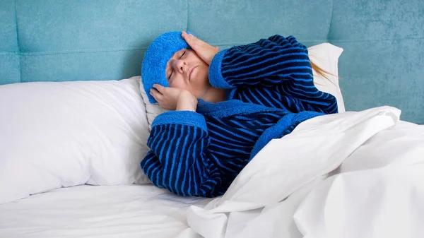 Retrato de mujer enferma con migraña acostada en la cama con toalla húmeda en la cabeza —  Fotos de Stock