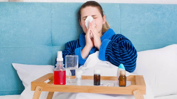 Retrato de mulher doente pegou frio deitado na cama e soprando corrimento nasal no tecido — Fotografia de Stock