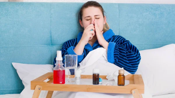 Portrait of sick woman with flu lying in bed and using nasal spray to stop runny nose — Stock Photo, Image