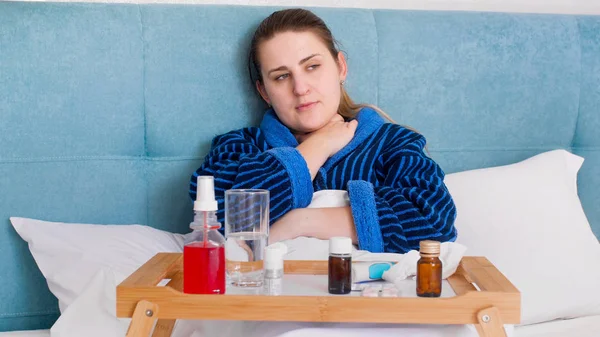 Retrato de una mujer enferma con gripe y fiebre acostada en la cama con una bandeja llena de pastillas y medicamentos —  Fotos de Stock